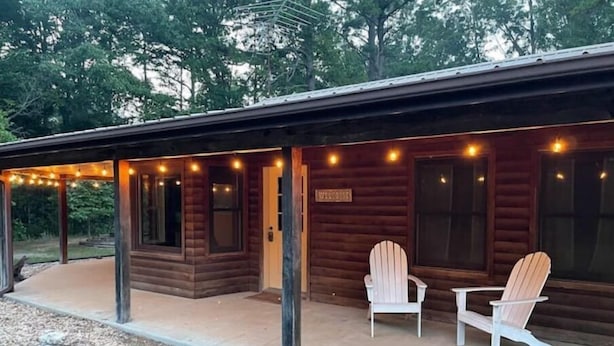 A wooden cabin with a porch, two Adirondack chairs, and a welcome sign.
