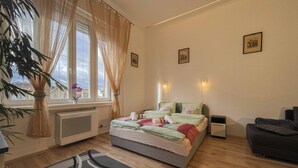 Ein Schlafzimmer mit einem Bett, Nachttischen, einem Fenster mit Vorhängen, einem Heizkörper, einer Pflanze und einem Sofa.
