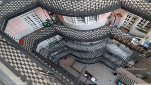 Ein mehrgeschossiges Gebäude mit Schachbrettmuster auf dem Boden, Balkonen und einem zentralen Innenhof.