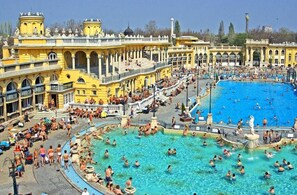 En stor udendørs swimmingpool omgivet af gule bygninger med klassisk arkitektur.