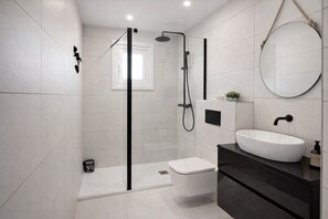 Une salle de bain moderne avec une douche à parois de verre, des toilettes blanches, un meuble-lavabo noir avec un évier blanc et un miroir rond.