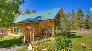 A log cabin with a green metal roof, surrounded by a well-maintained garden with various plants and flowers.