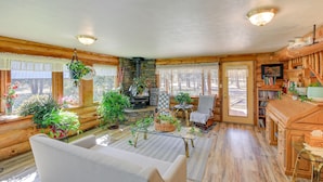 A cozy cabin interior with a sofa, a fireplace, wooden walls, and large windows.
