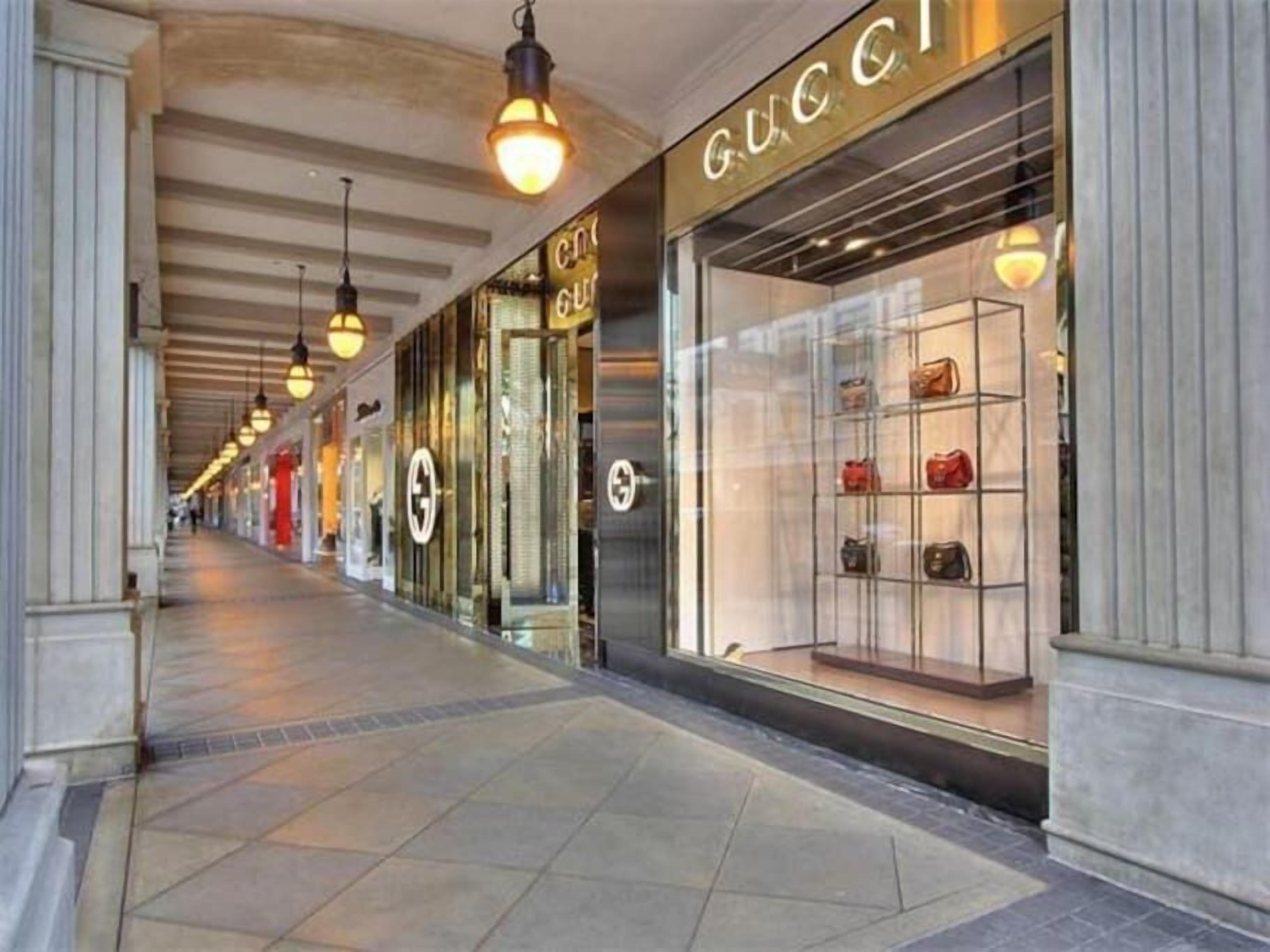 A corridor with storefronts, including a Gucci store with a display of handbags.