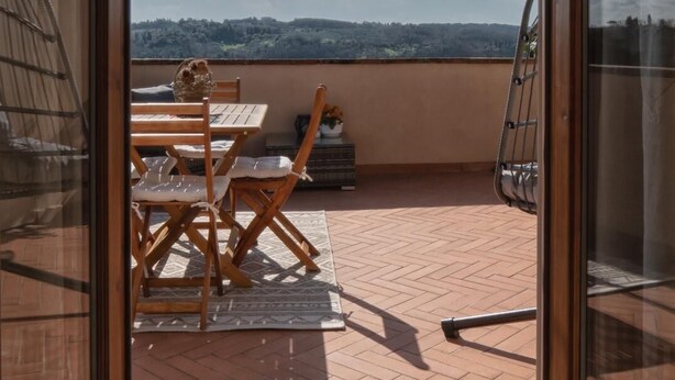 Un balcon avec une table et des chaises, un pot de fleurs et une vue sur le paysage.