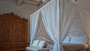 Un lit à baldaquin à quatre poteaux avec une literie et des oreillers blancs, une commode en bois et un banc avec des coussins.