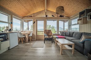 A spacious living area with a wooden ceiling, large windows, a sofa, a coffee table, and a dining table with chairs. - Sel Lodge next to Geysir and Gullfoss. Right in the Golden Circle. (selfoss)