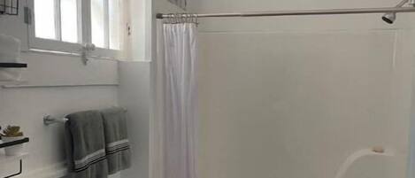 Een badkamer met een bad, douche, wastafel en raam.
