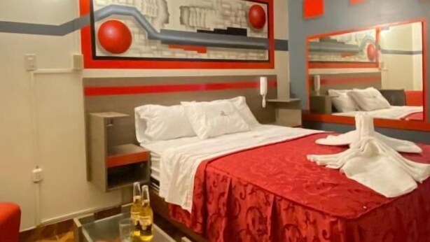 A hotel room with a bed, bedside table, and a mirror. - HOSTAL BERMUDAS (Lima)