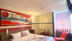 A hotel room with a large bed, a desk, a chair, and a TV.