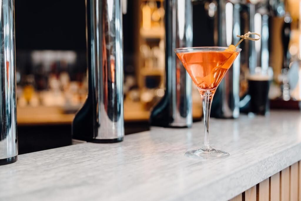 Um copo de martini com uma bebida alaranjada em um balcão de bar.