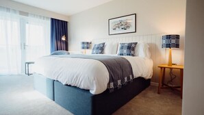 Um quarto moderno com uma cama grande, uma mesa de cabeceira com abajur e um quadro na parede.