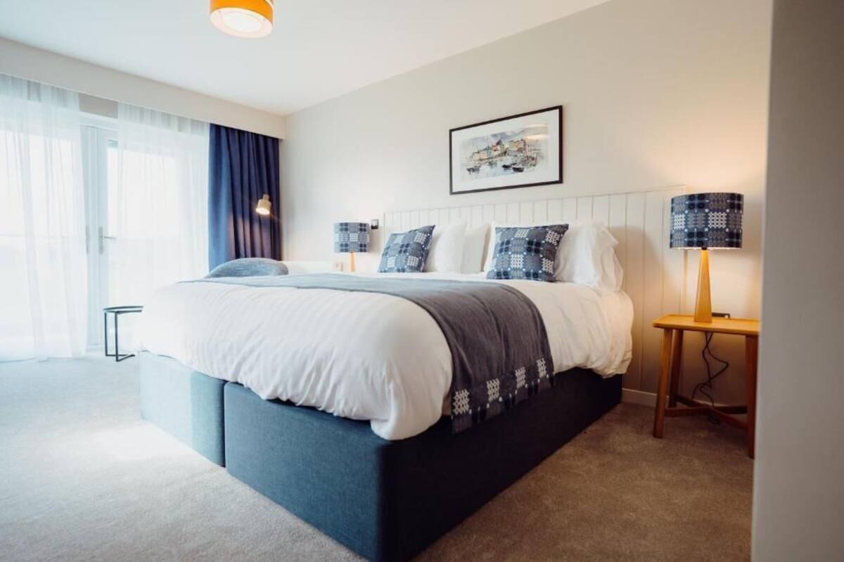 Um quarto moderno com uma cama grande, uma mesa de cabeceira com abajur e um quadro na parede.