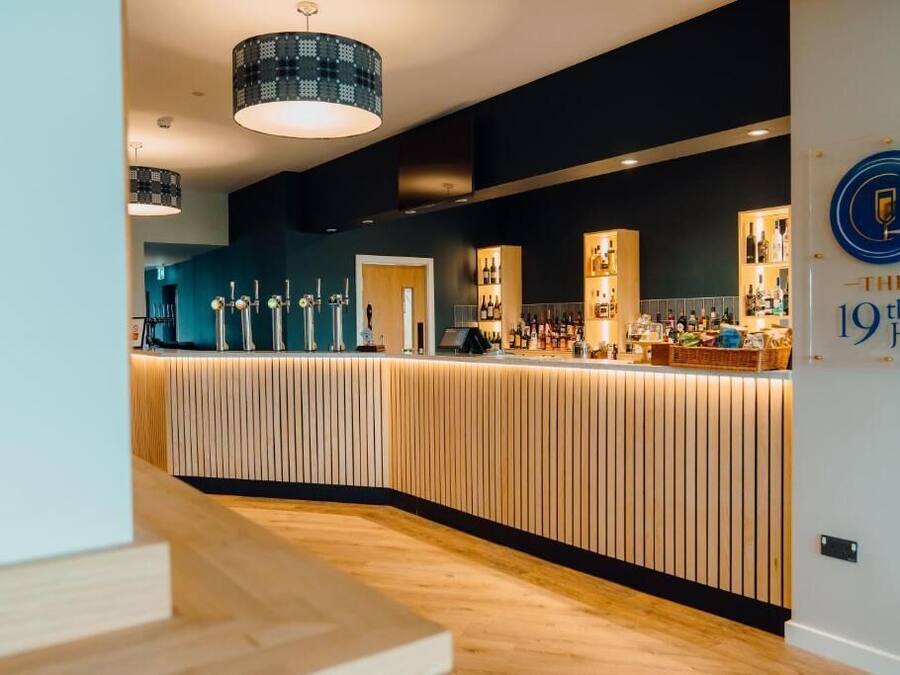 Eine moderne Bar mit Holztresen, Pendelleuchten und einem Schild mit der Aufschrift "The 19th Hole".
