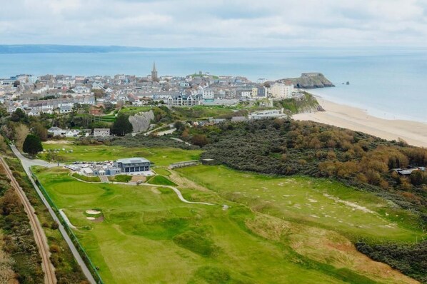 An aerial view of a coastal town with a beach, a golf course, and a prominent church spire.