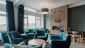 Uma área de estar moderna com poltronas azul-turquesa, uma mesa redonda de madeira e um painel decorativo na parede.