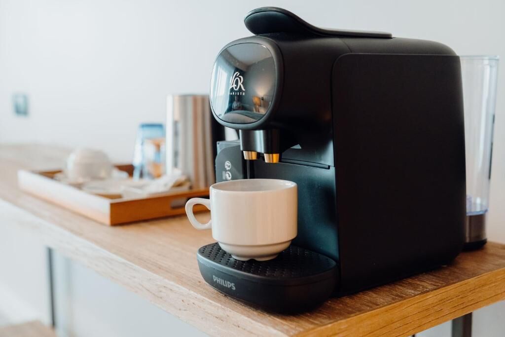 A black coffee maker with a white cup on its base, placed on a wooden table.