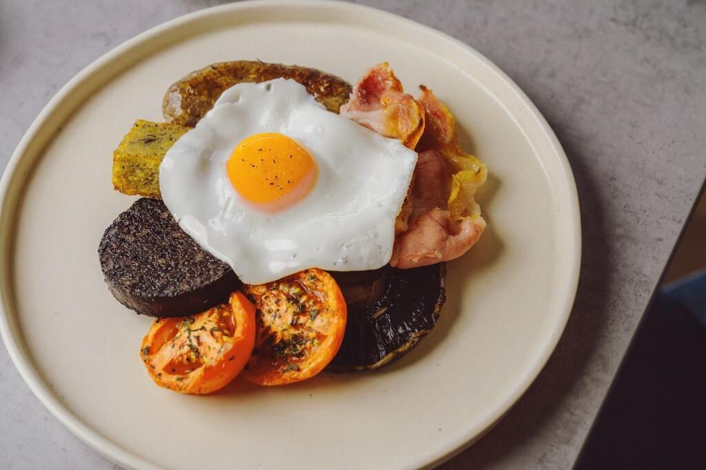 A plate with a fried egg, bacon, black pudding, and grilled tomatoes.