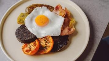 Un plato con un huevo frito, bacon, morcilla y tomates a la parrilla.