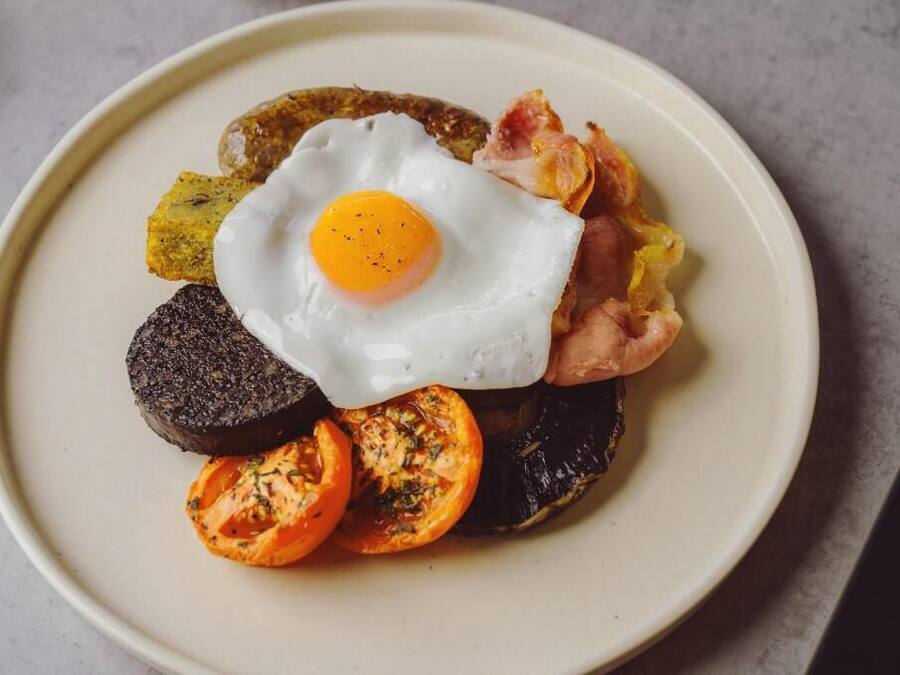 A plate with a fried egg, bacon, black pudding, and grilled tomatoes.