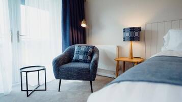 A hotel room with a bed, a chair, a small table, a lamp, and a view of the outdoors.