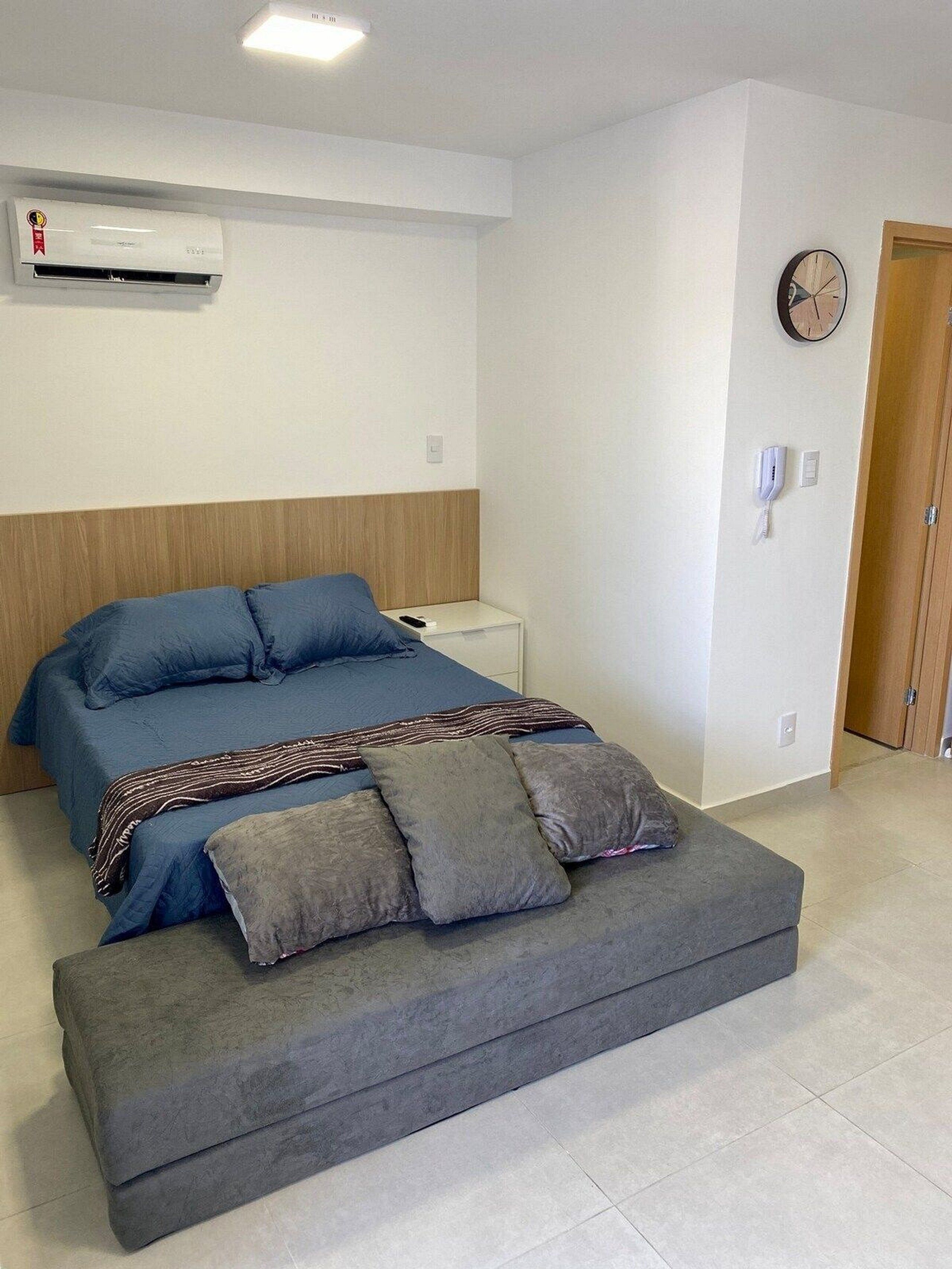 Een slaapkamer met een bed, nachtkastje en een wandairconditioner.
