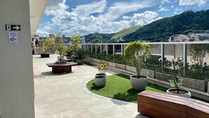 Una terrazza sul tetto con vista su una città e delle colline, con fioriere piene di piante, una panca di legno e un segnale Wi-Fi.