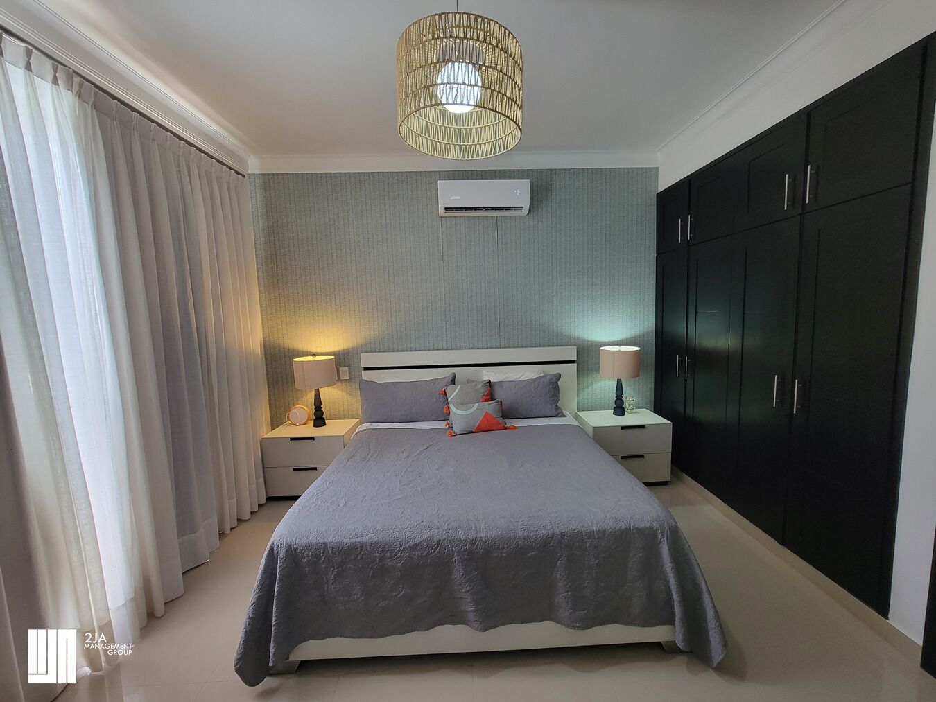Ein Schlafzimmer mit Bett, Nachttischen, einer Lampe, einer Klimaanlage und einem Kleiderschrank.
