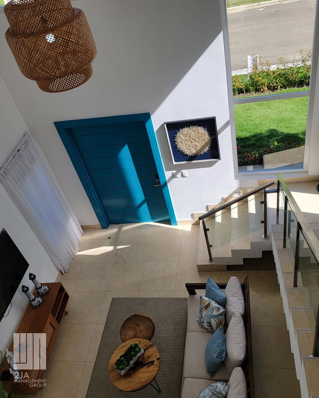 A modern living room with a blue door, a mounted artwork, a staircase, and a view of a green lawn.