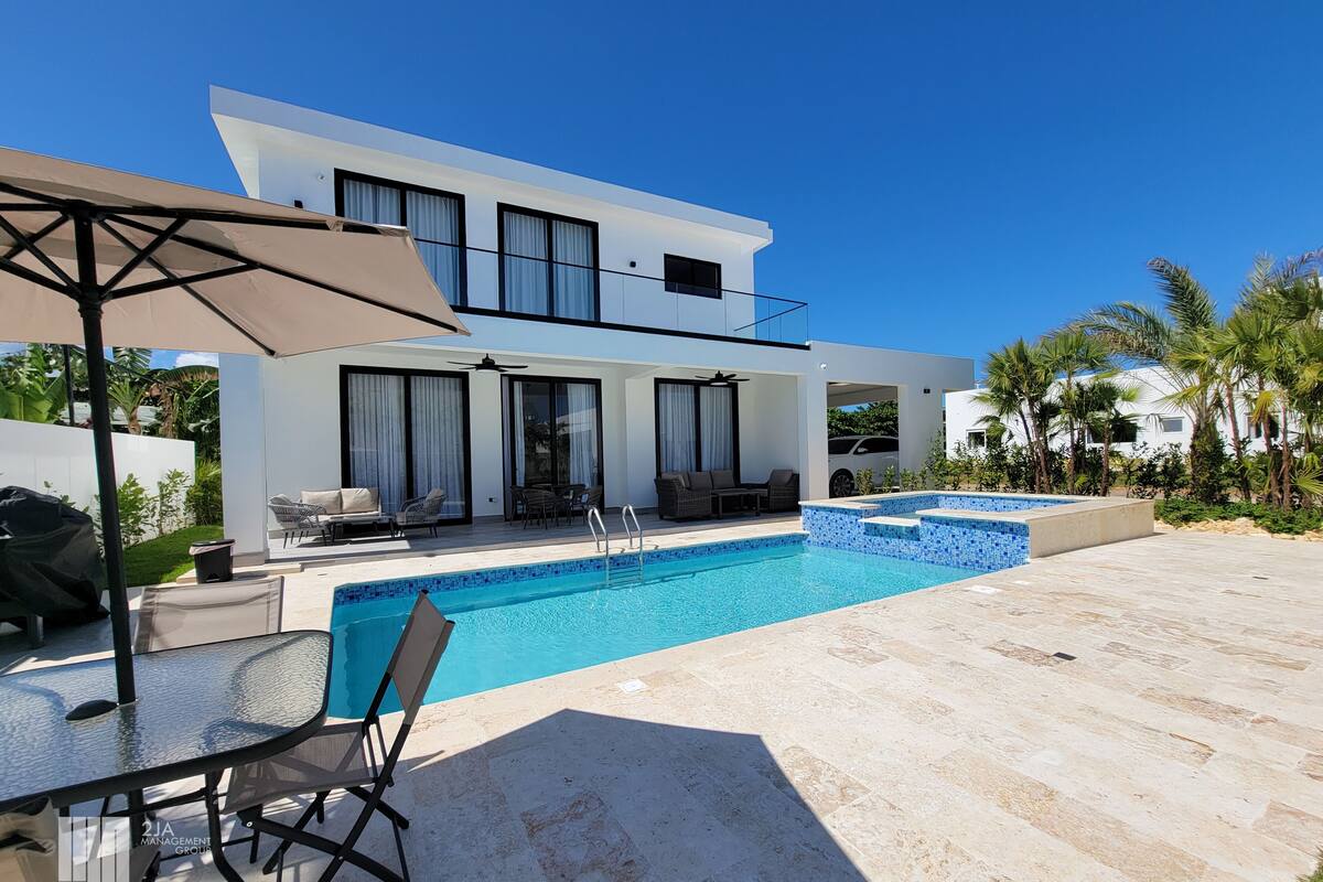 A modern two-story house with a swimming pool, outdoor seating, and a view of the surrounding landscape.