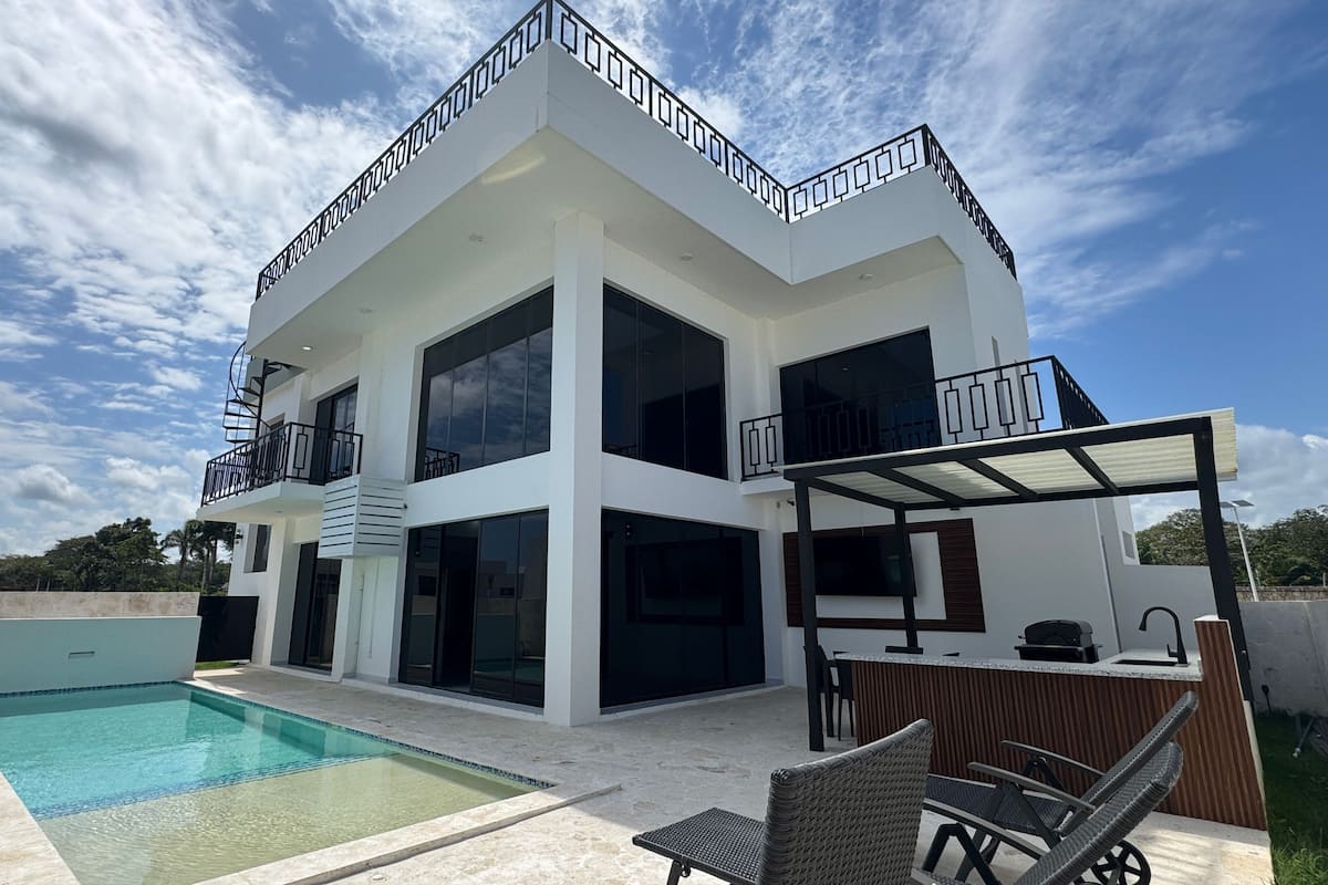 A modern two-story house with a swimming pool, outdoor seating, and a balcony.