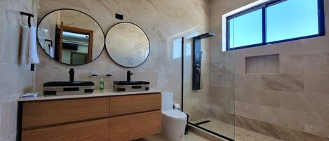 Une salle de bain moderne avec deux lavabos, un meuble-lavabo, une douche et une grande fenêtre.