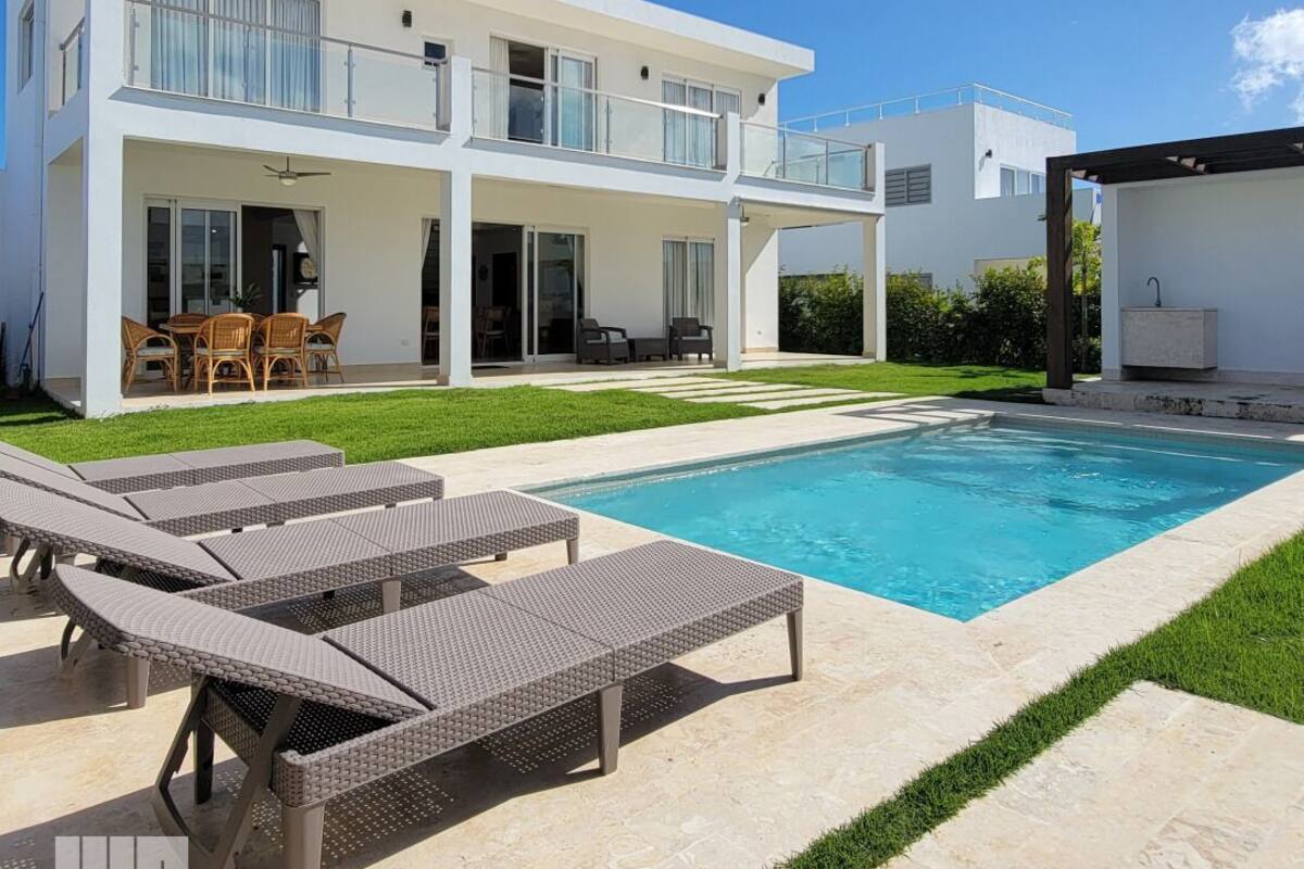 A modern two-story house with a swimming pool, outdoor furniture, and a well-maintained lawn.