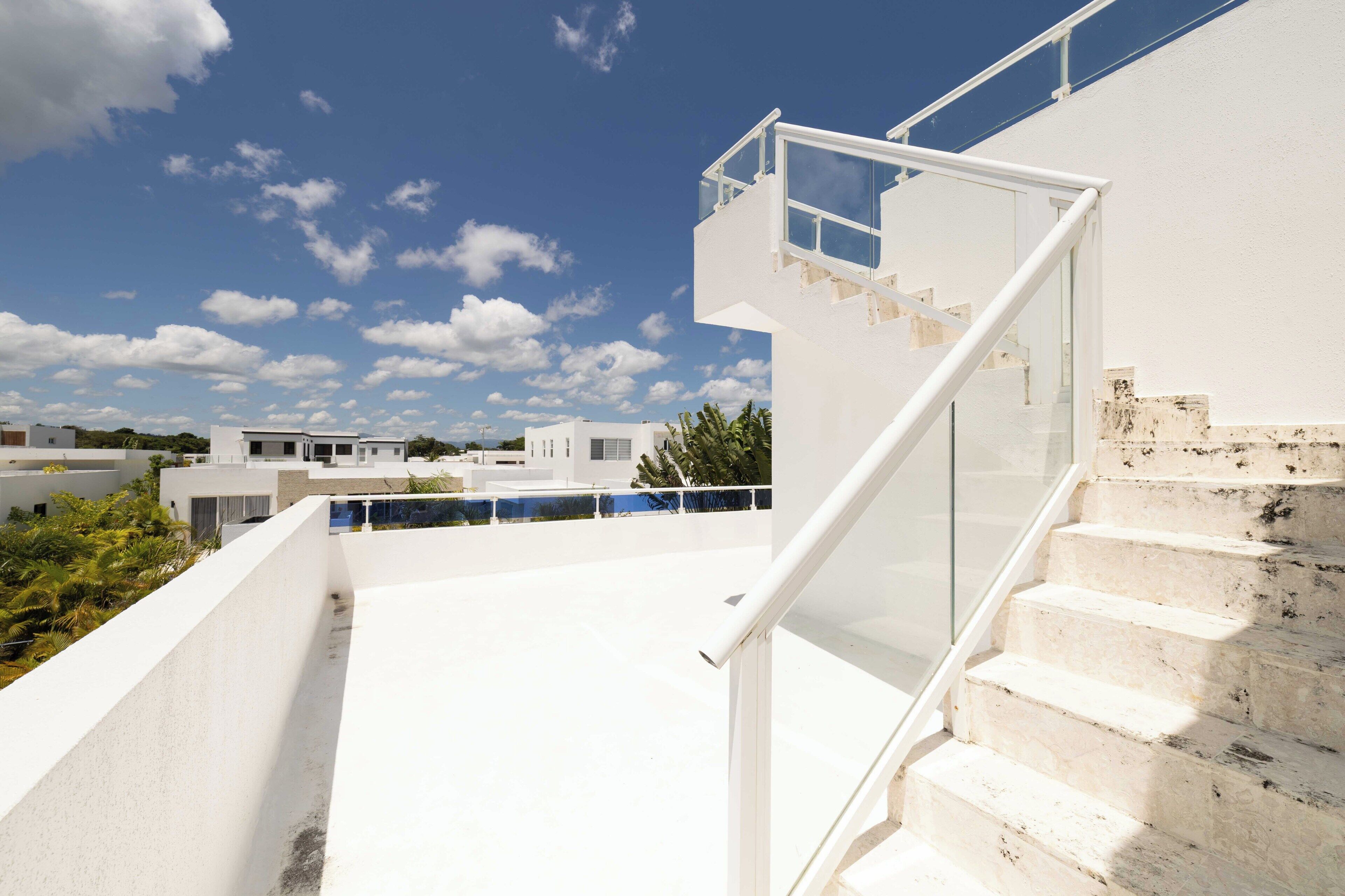 Een modern gebouw met een witte gevel, een glazen trap en een helderblauwe lucht met wolken.