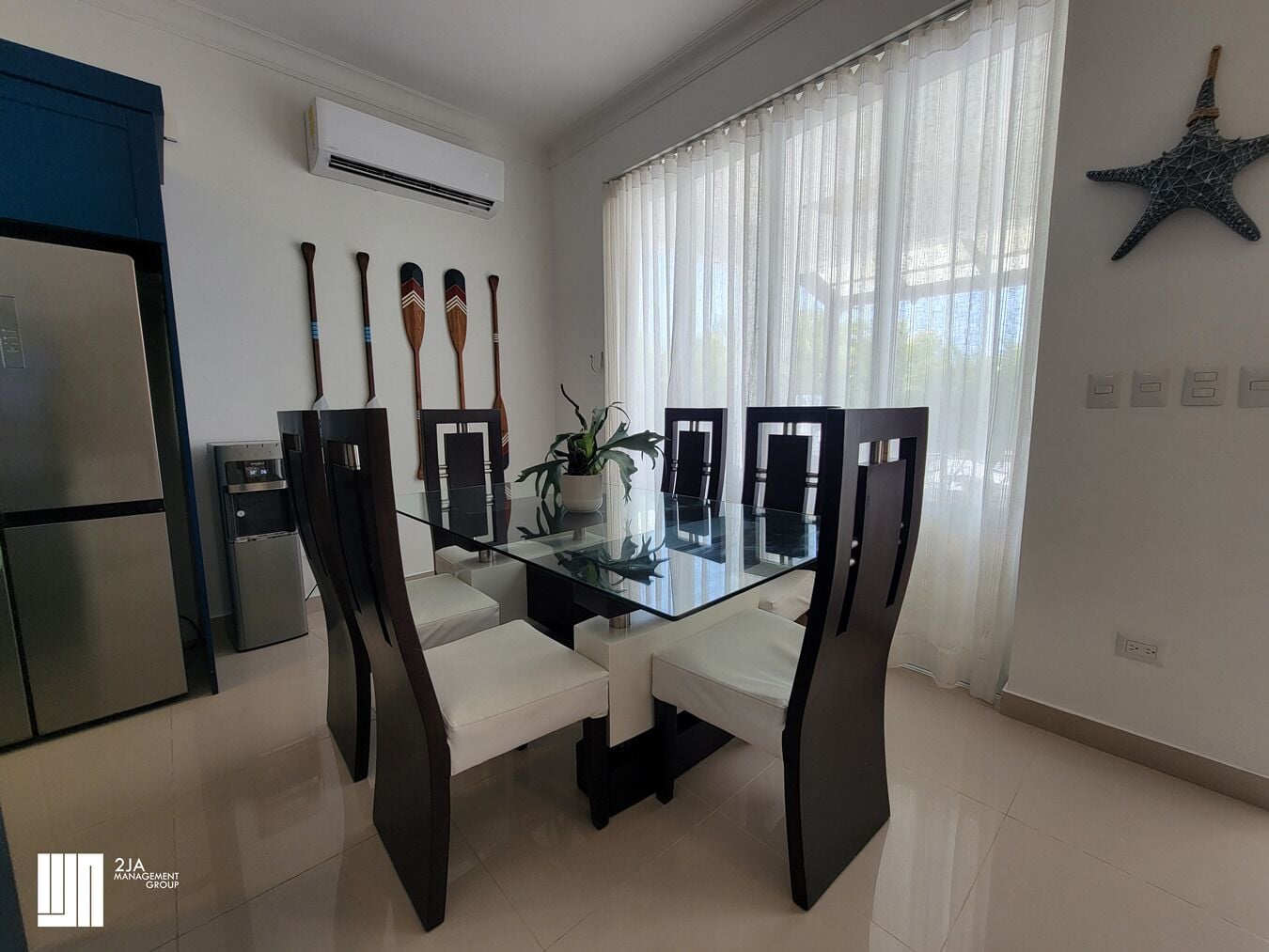 Un espace repas moderne avec une table en verre, des chaises noires, une plante en pot et une décoration en forme d’étoile de mer.