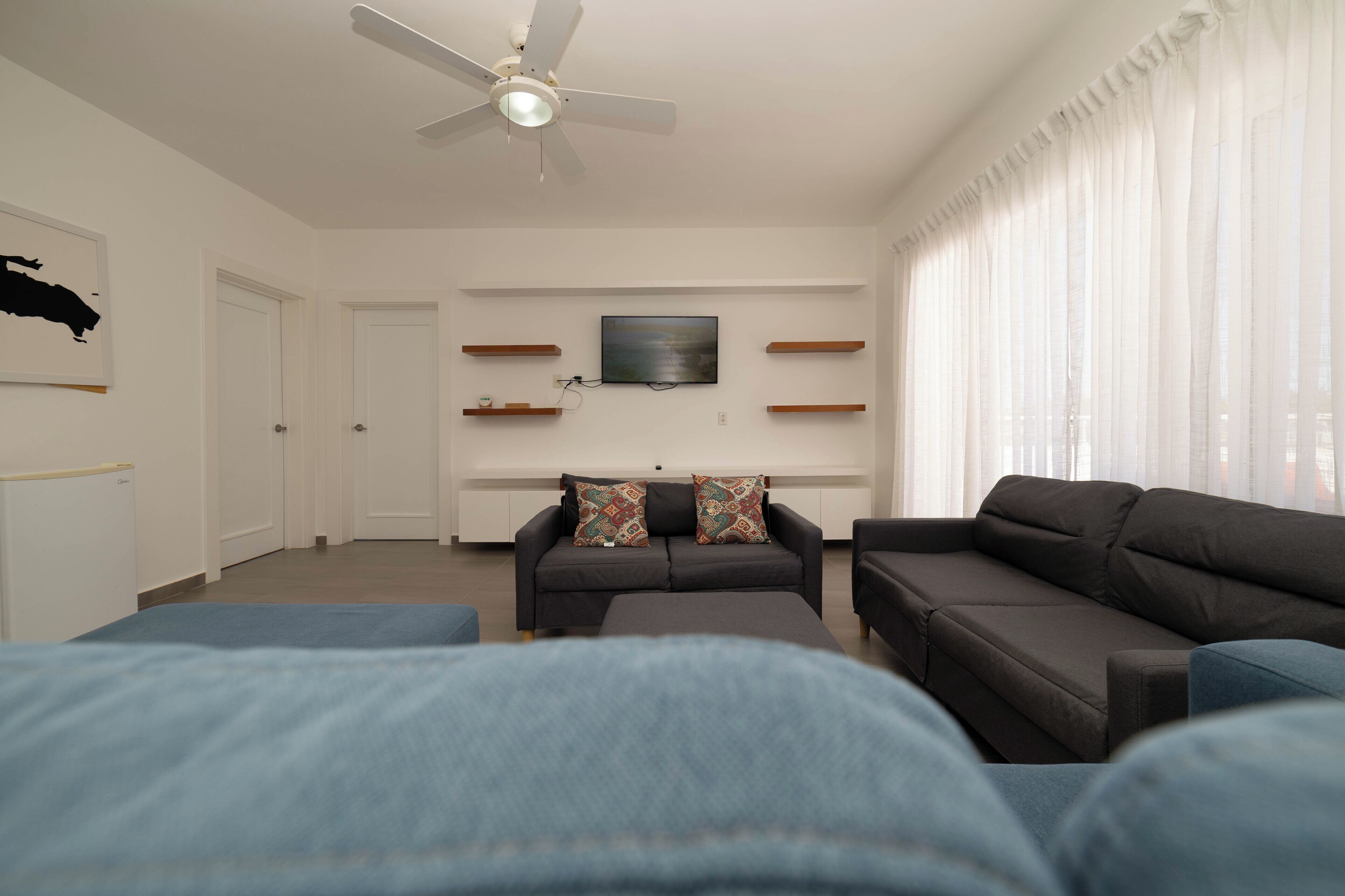 A modern living room with a ceiling fan, a flat-screen TV mounted on the wall, and a sofa with patterned cushions.