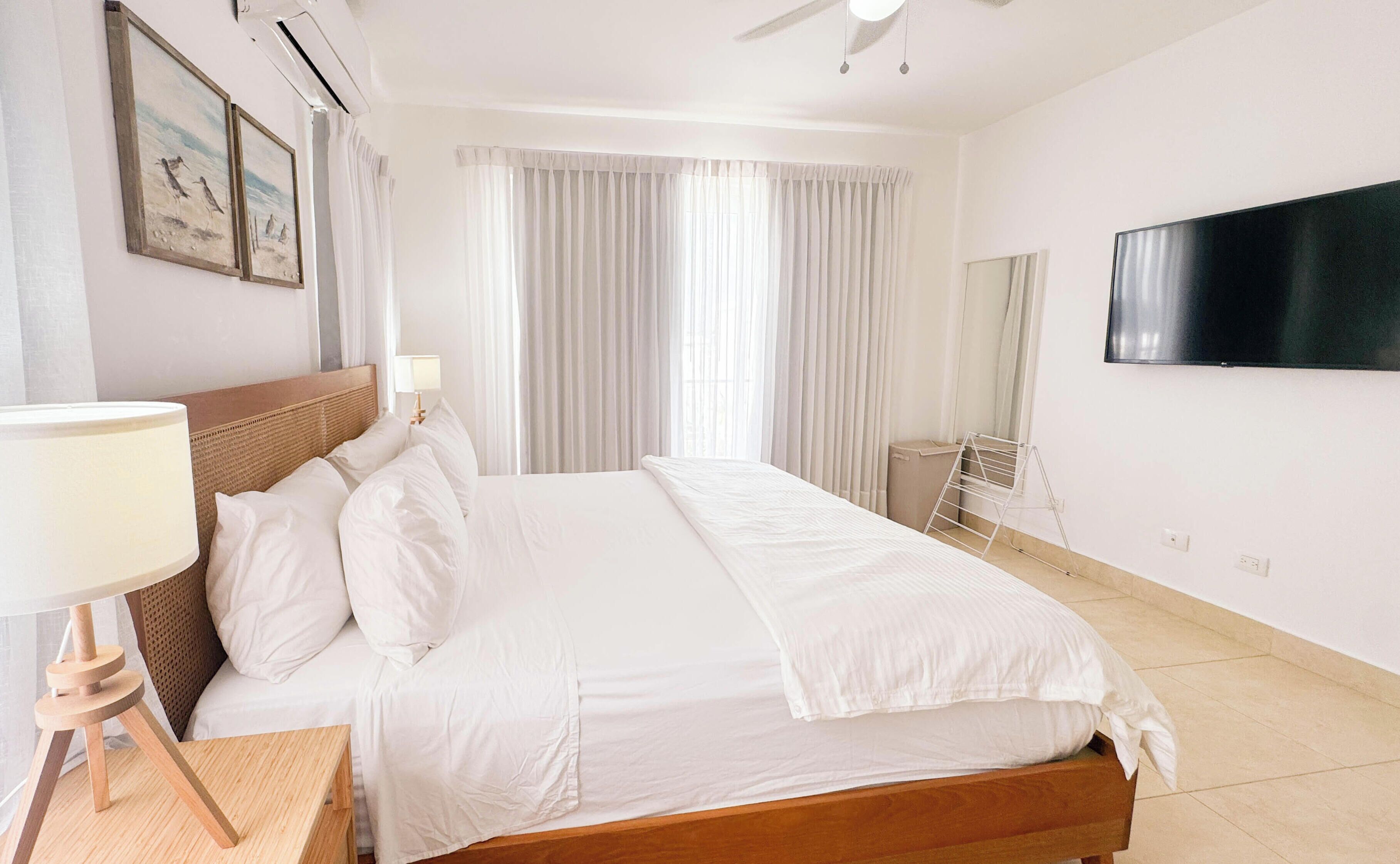 Een hotelkamer met een bed, een aan de muur bevestigde televisie en een raam met gordijnen.