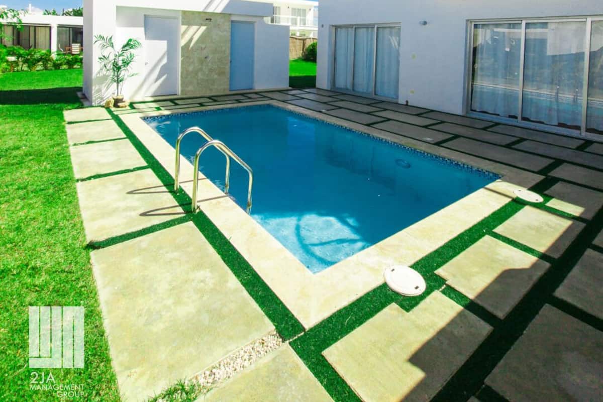 A modern residential building with a swimming pool, a covered patio, and a well-maintained lawn.