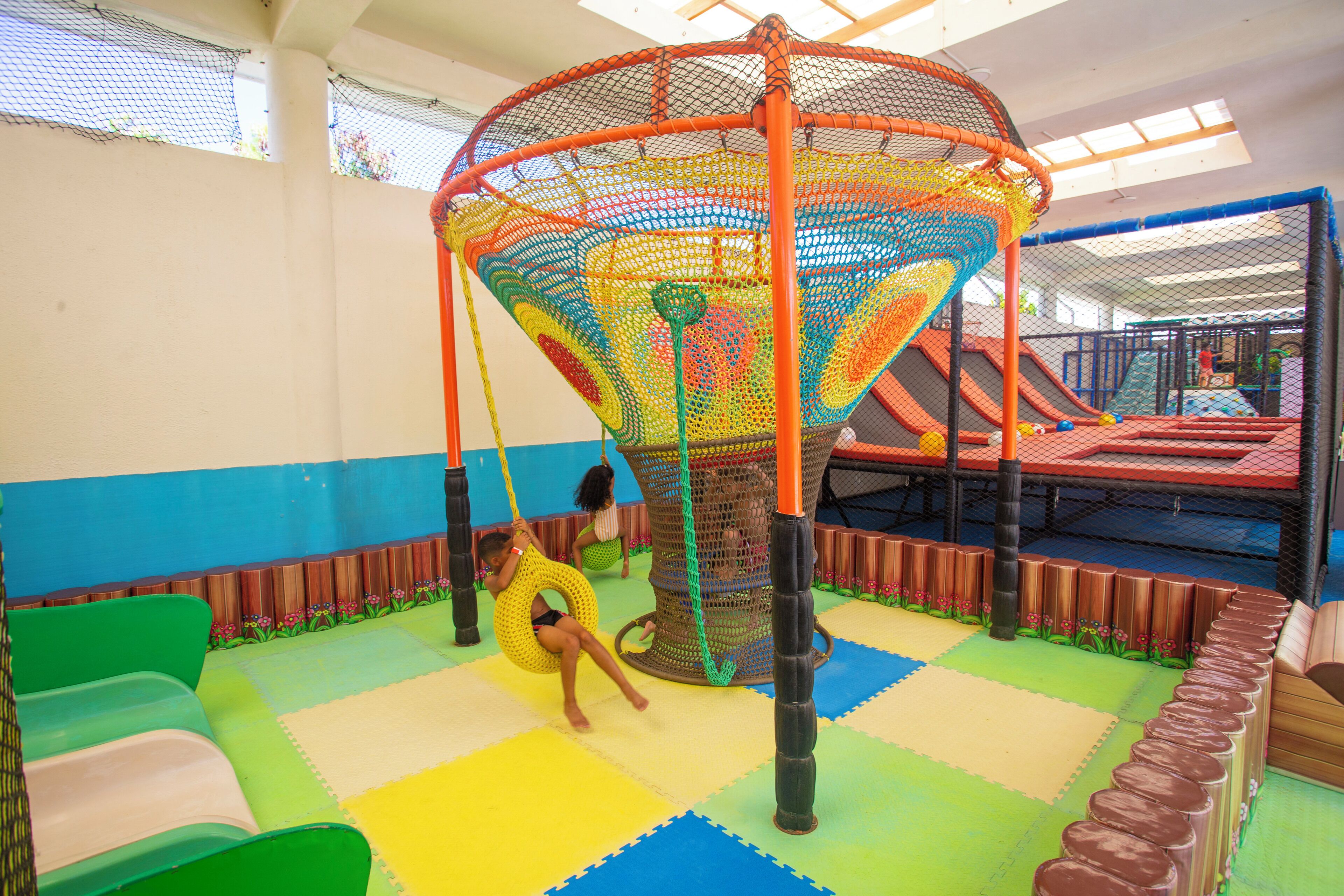 A play area with a netted climbing structure, a slide, and padded flooring.