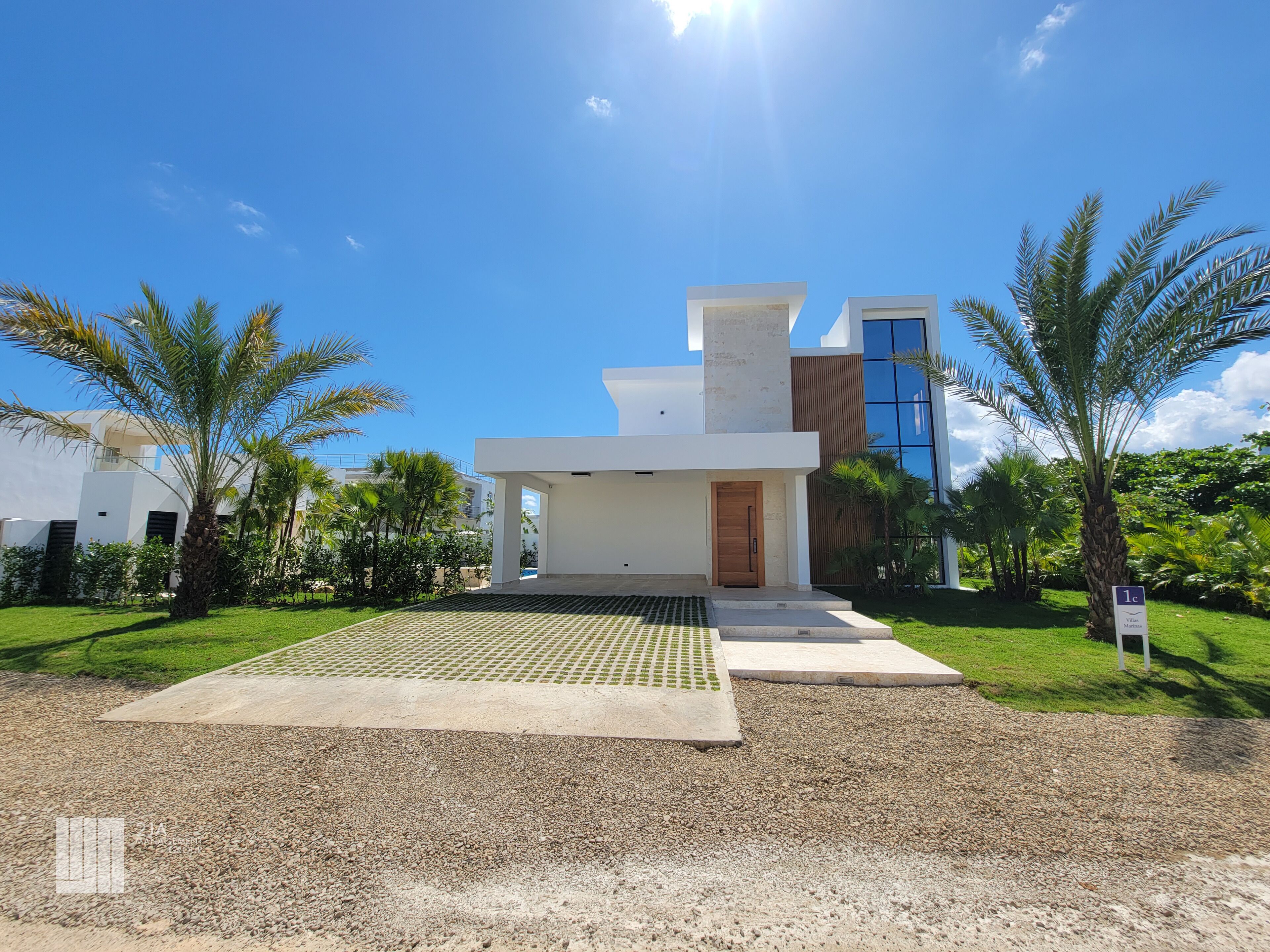 A modern villa with a spacious patio, palm trees, and a clear blue sky.