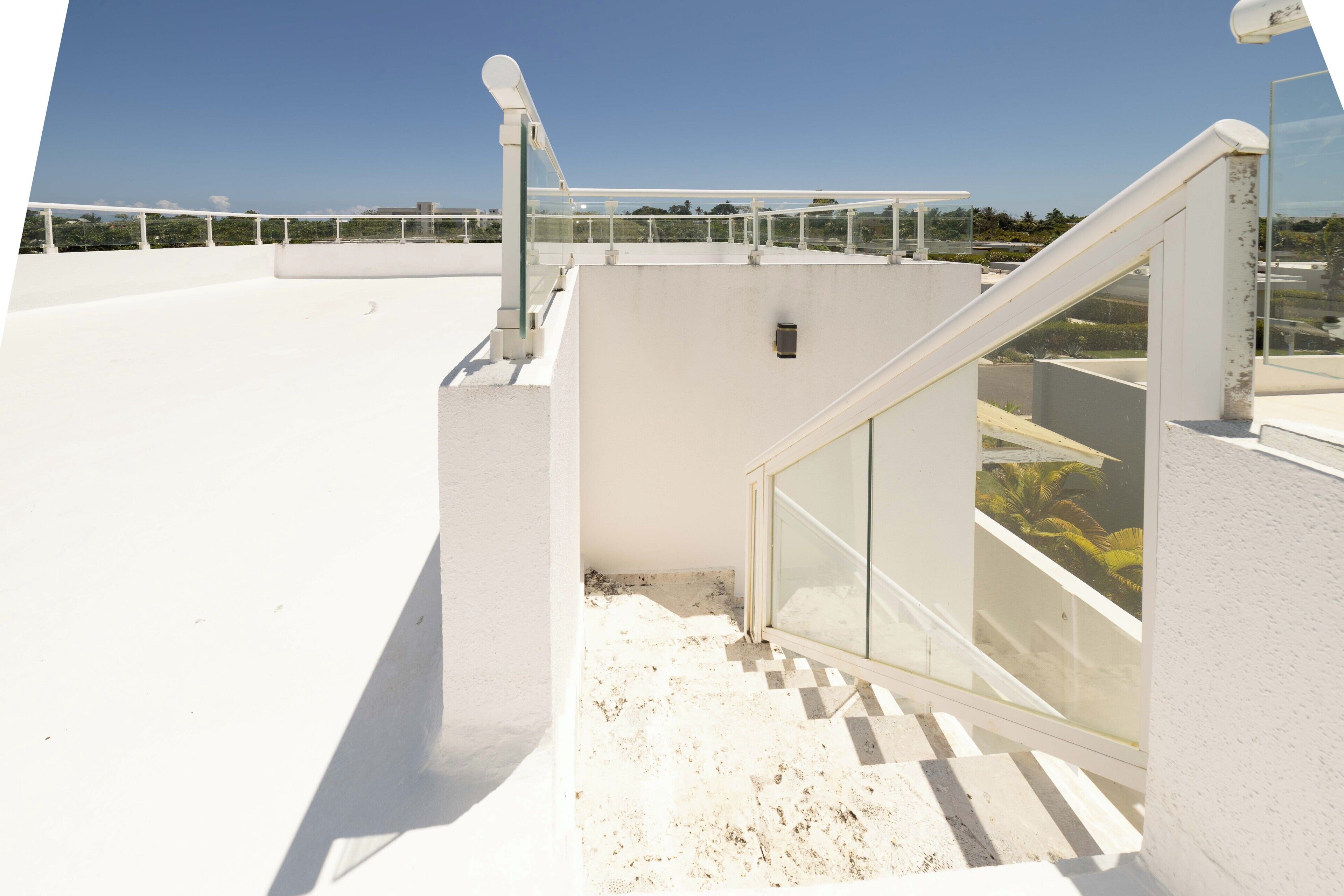 Una terraza en la azotea con barandilla de vidrio y pasamanos blanco, bajo un cielo despejado.