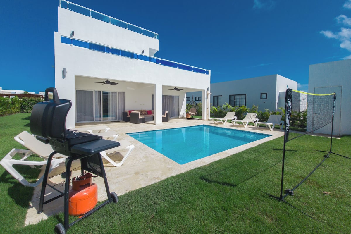 A modern house with a pool, outdoor seating, and a barbecue grill.