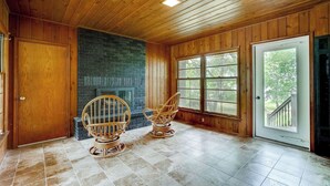 A room with wooden walls, a fireplace, two wicker chairs, and a large window. - Midcentury Lake Home! (White Bear Lake)