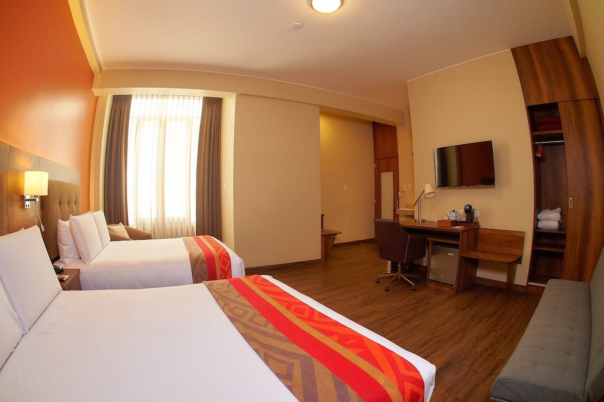 Une chambre d’hôtel avec deux lits, un bureau, une télévision et un coin salon.