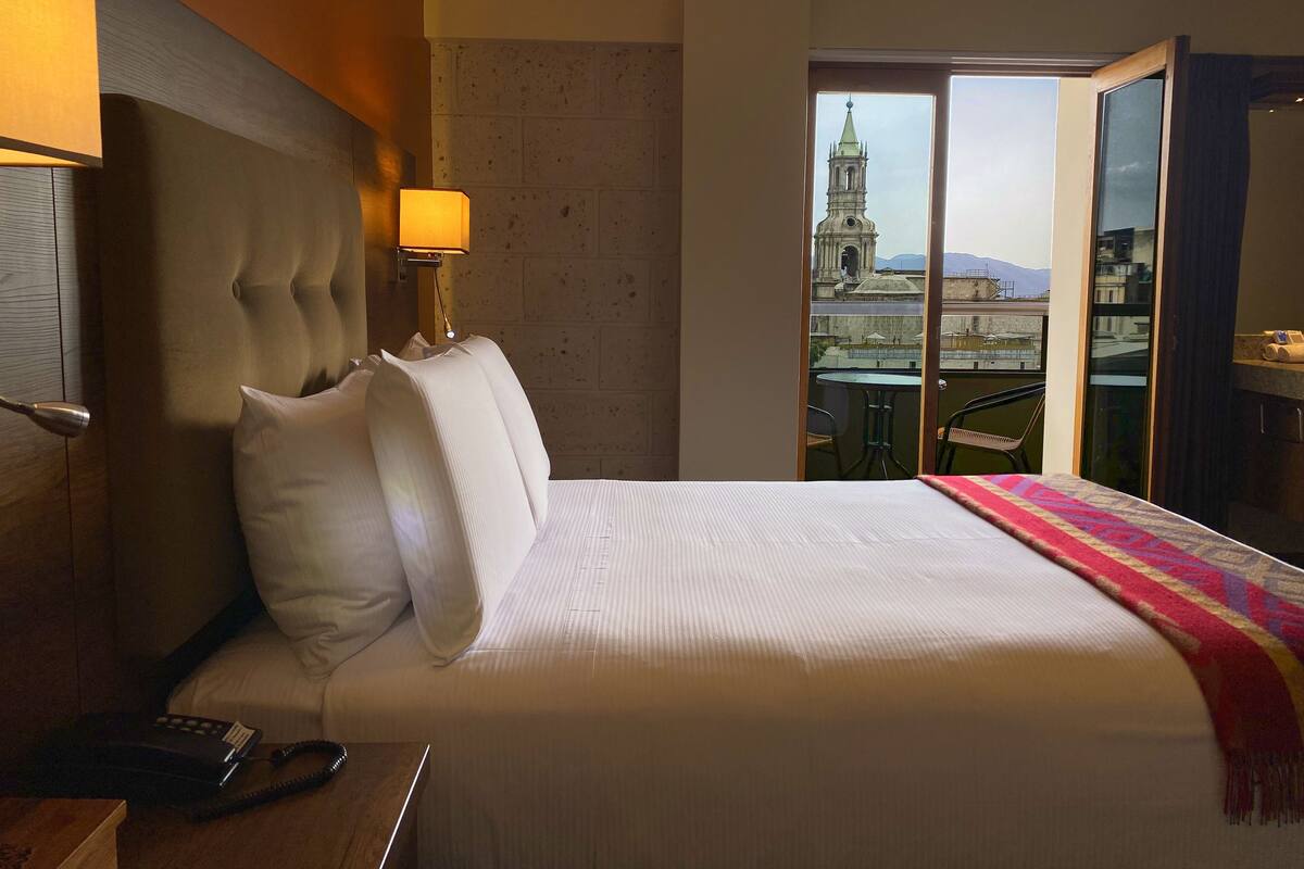 Une chambre d’hôtel avec un grand lit, une lampe de chevet, un téléphone et une vue sur le paysage urbain, avec une tour en particulier.