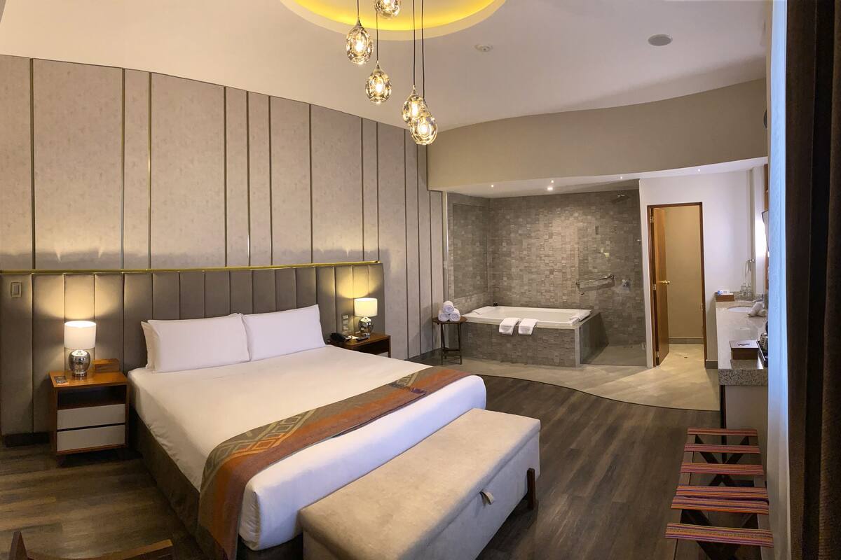 Une chambre d’hôtel moderne avec un grand lit, des lampes de chevet, une salle de bain avec baignoire et douche.