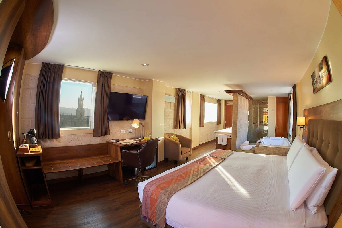 Une chambre d’hôtel avec un grand lit, un bureau, une chaise, une télévision et une vue sur une tour par la fenêtre.