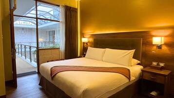 Habitación de hotel con una cama grande, una mesita de noche, una lámpara y vistas al balcón exterior.