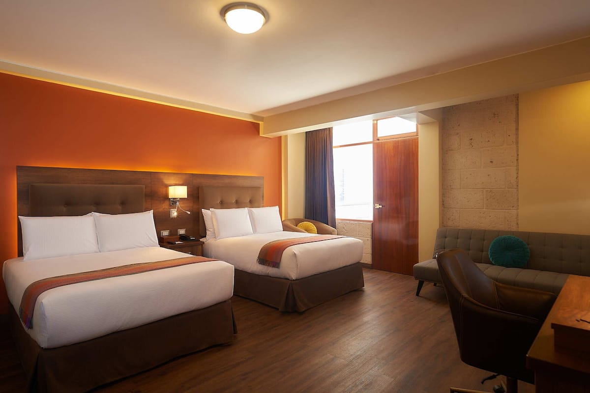Une chambre d’hôtel avec deux lits, un canapé, un bureau et une fenêtre avec des rideaux.