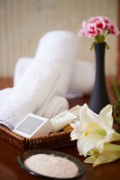 A basket with folded towels, a vase with pink flowers, and a small bowl of bath salts.